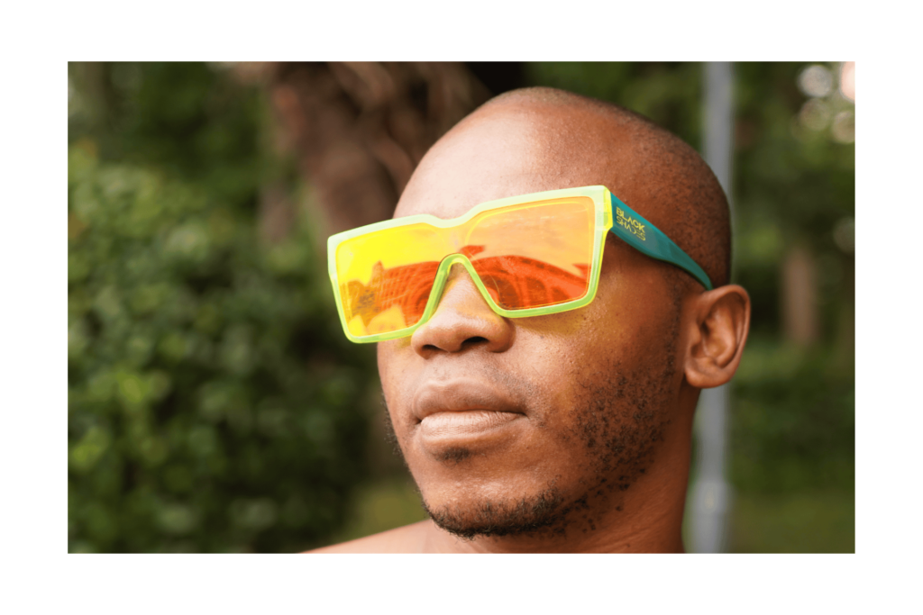 A man gazes wearing Hangover Harbor sunglasses by Black Shades, a neon green frame with neon pink lenses.